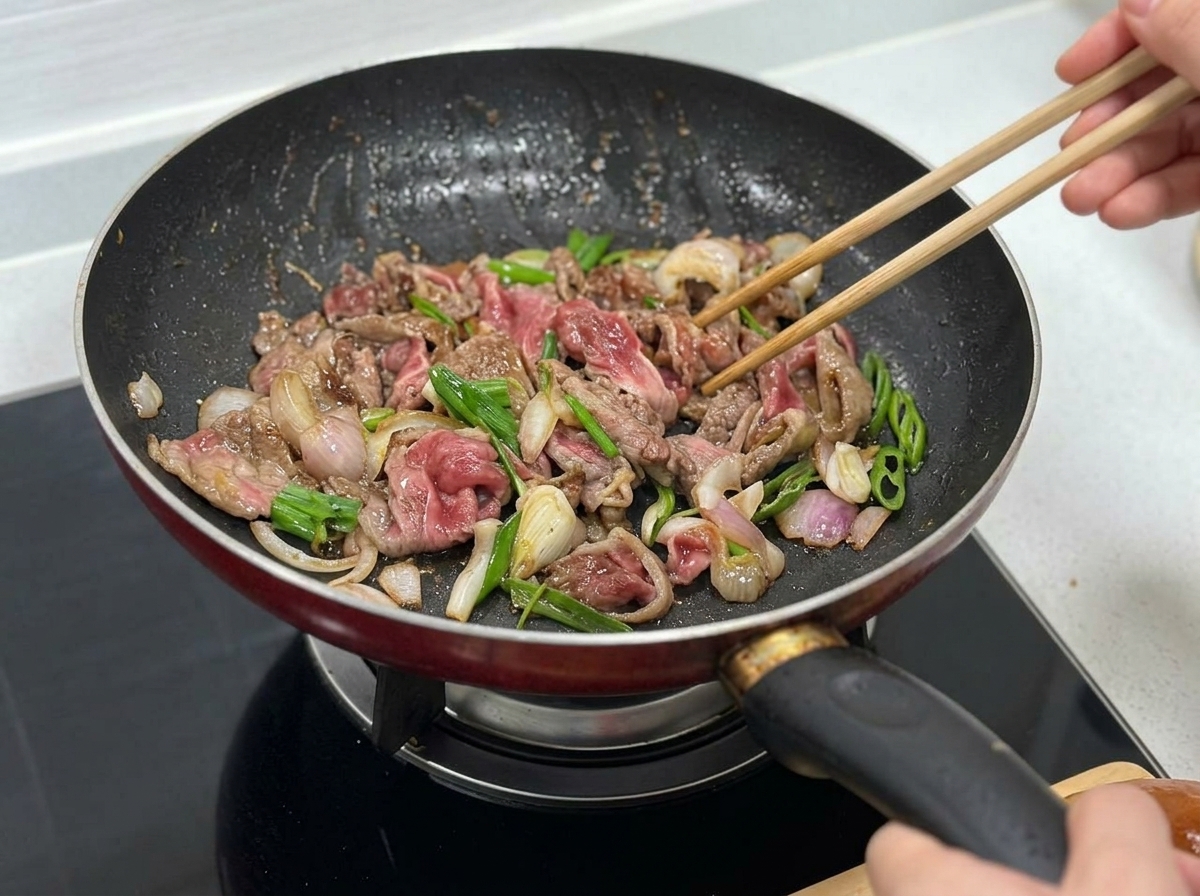 Rindfleisch, Zwiebeln und grüne Paprikastreifen werden zusammen angebraten.