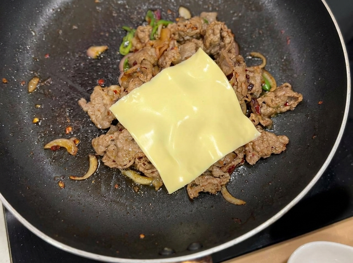 Eine Scheibe gelber Käse schmilzt auf der Fleischmischung.
