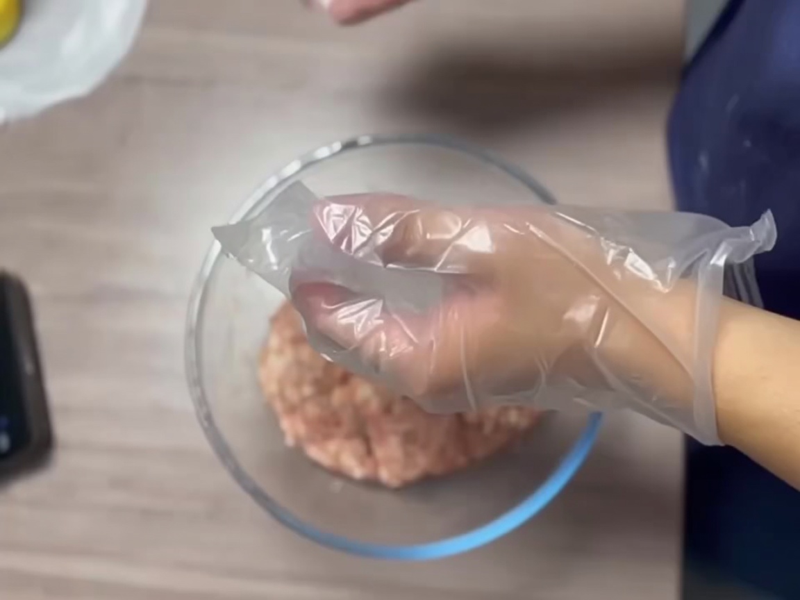 Gehandschuhte Hände formen Fleisch zu einer glatten Kugel.