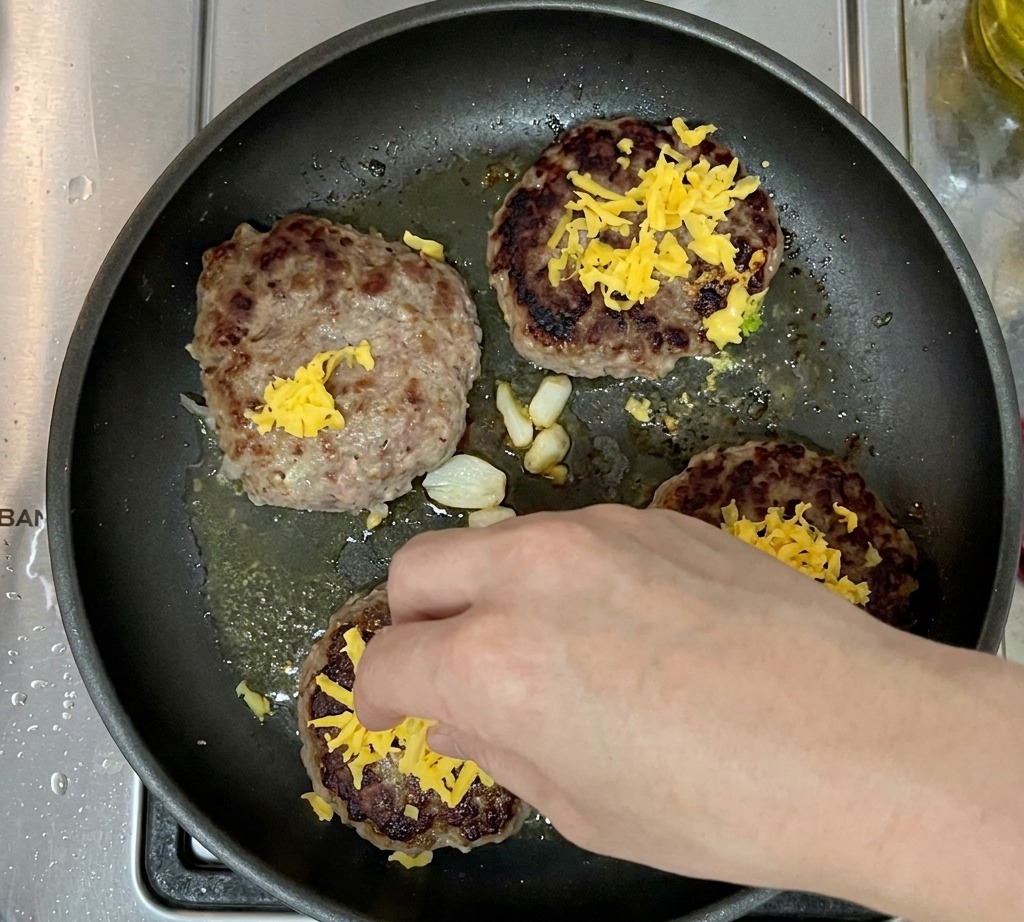 Gebratene Patties mit schmelzendem Cheddar in der Pfanne.