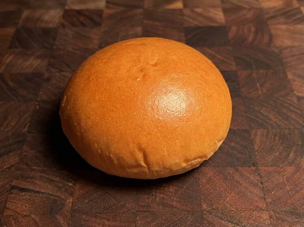 Ein goldbraun getoastetes Burgerbrötchen auf einer Holzunterlage.