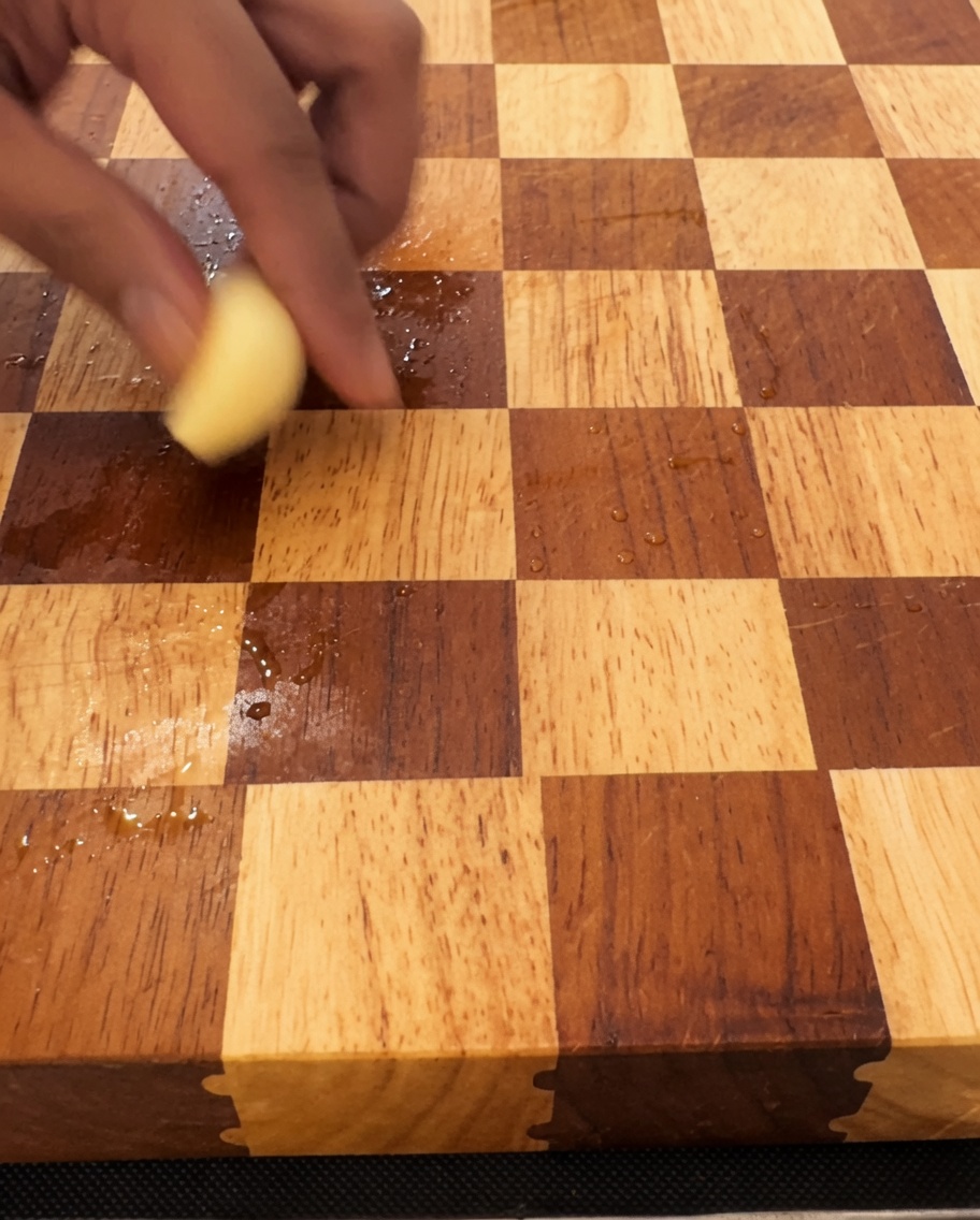 Knoblauchzehen werden auf einem Holzschneidebrett mit einem großen Messer fein gehackt.