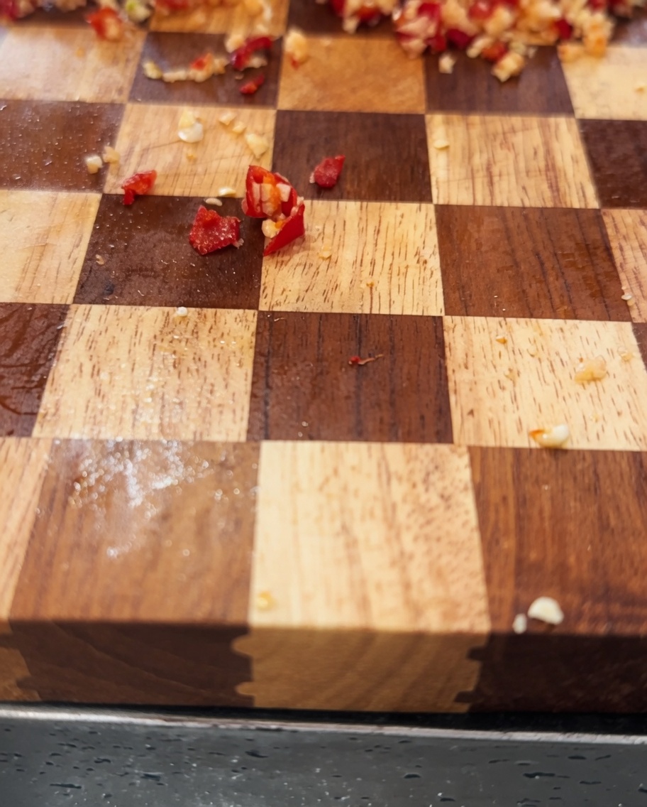 Eine Mischung aus gehacktem Knoblauch und roten Chilis wird in einer Edelstahlschüssel mit Olivenöl vermischt.