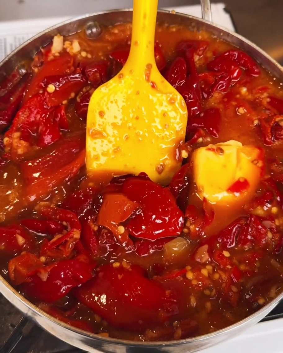 Die Chilisauce köchelt in einer Pfanne, während eine dicke, dunkle Sauce eingerührt wird, was für ein reichhaltiges und glänzendes Finish sorgt.