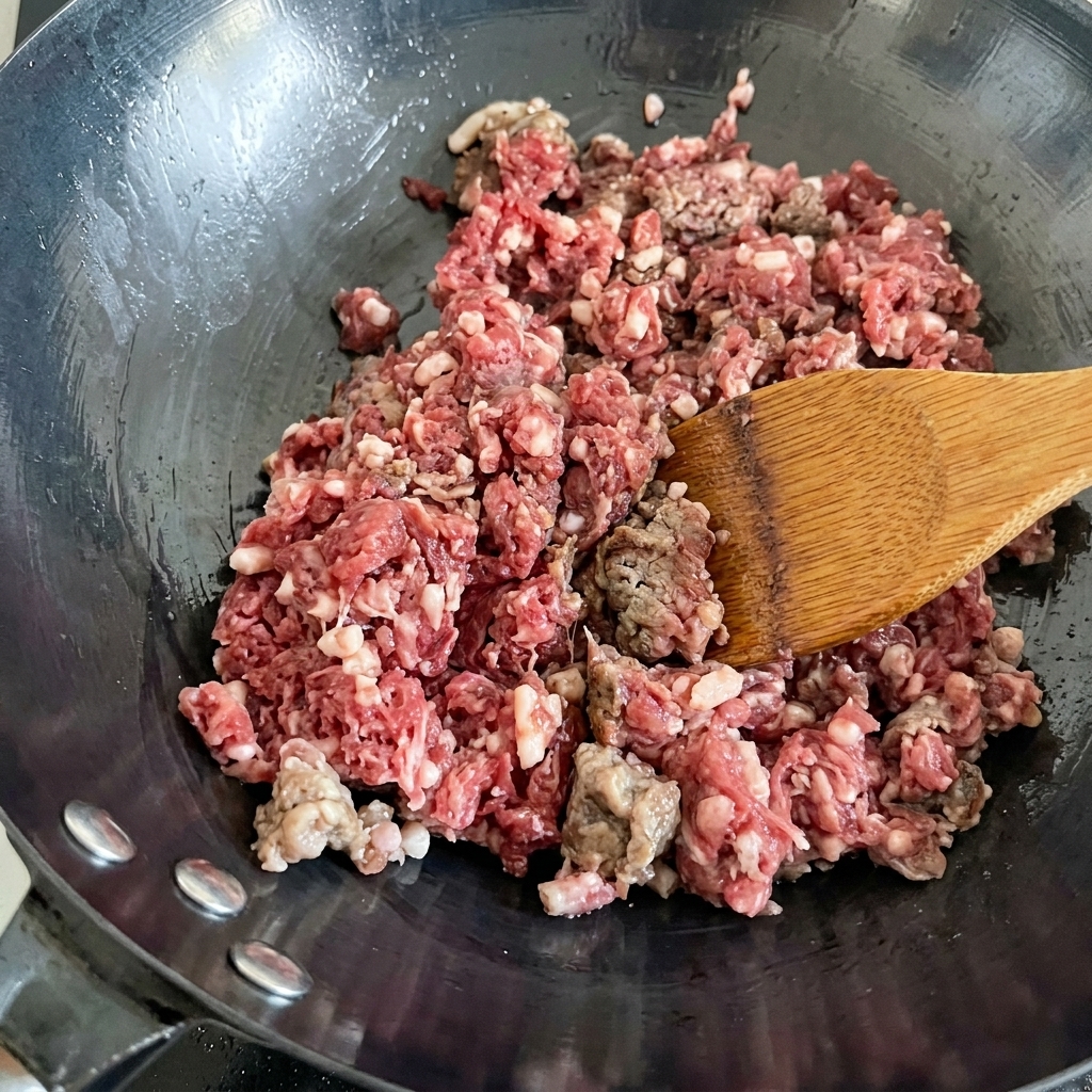 Frisches Rinderhackfleisch wird in einem heißen Wok angebraten und verfärbt sich von Rot zu Braun.
