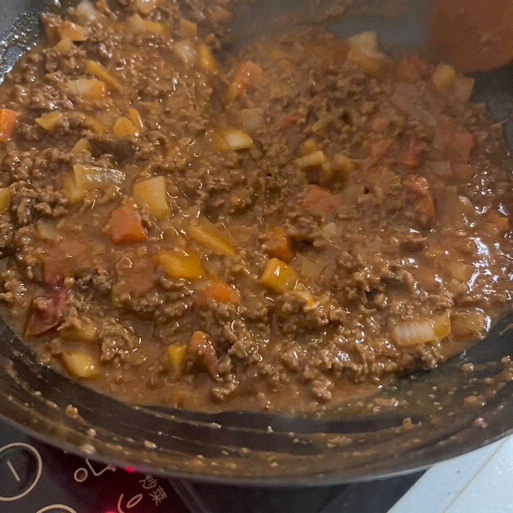 Eine dunkle, reichhaltige Sauce wird unter die Fleisch-Gemüse-Mischung im Wok gerührt.