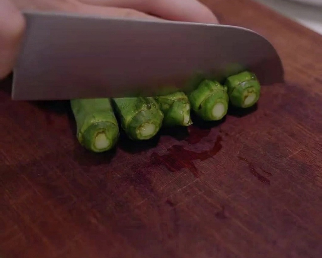 Frische grüne Okra, die auf einem Holzbrett in kleine Scheiben geschnitten wird.