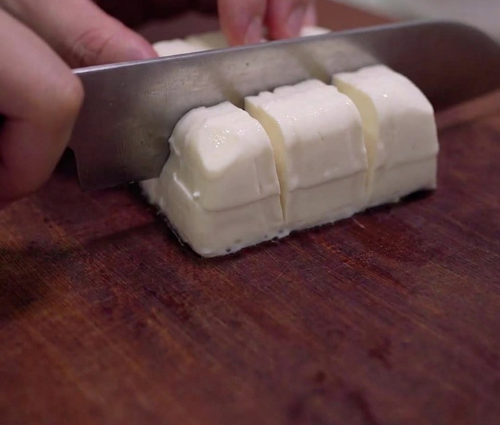Ein Block seidiger Tofu, der sorgfältig in kleine Würfel auf einem Holzbrett geschnitten wird.