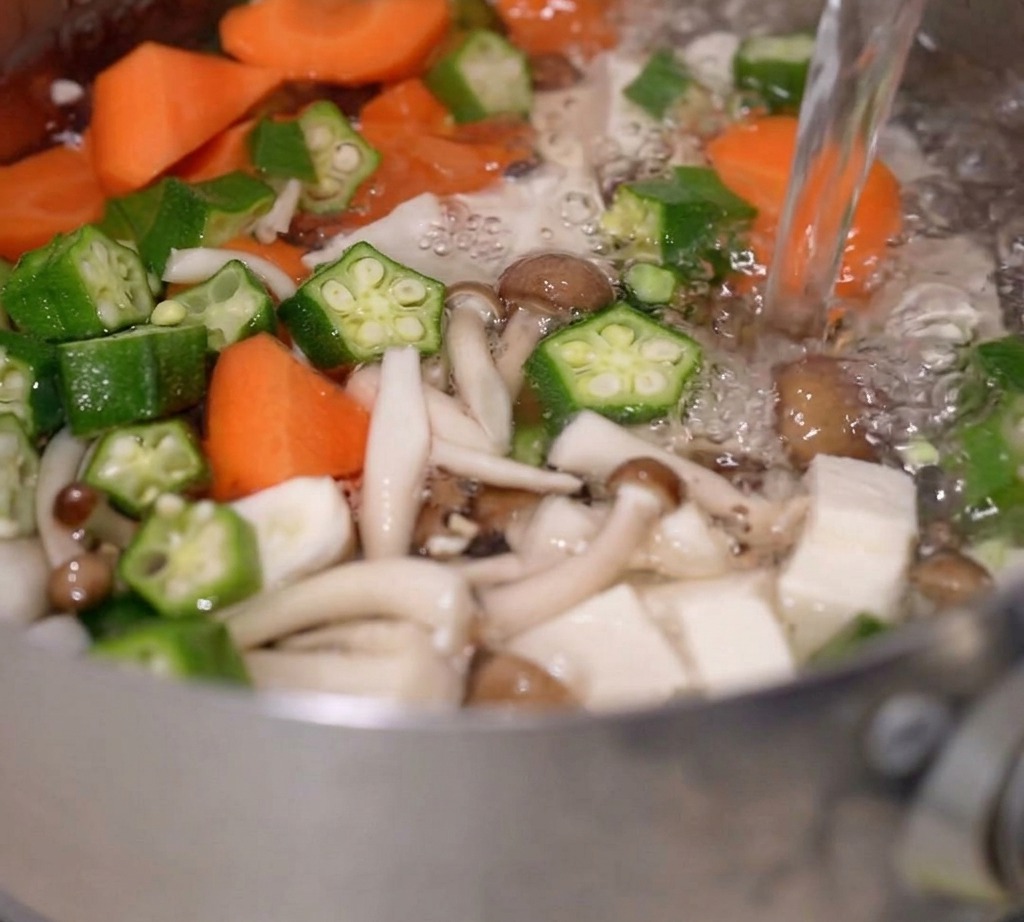Kochendes Wasser wird in einen Topf mit gemischtem Gemüse und Tofu gegossen.