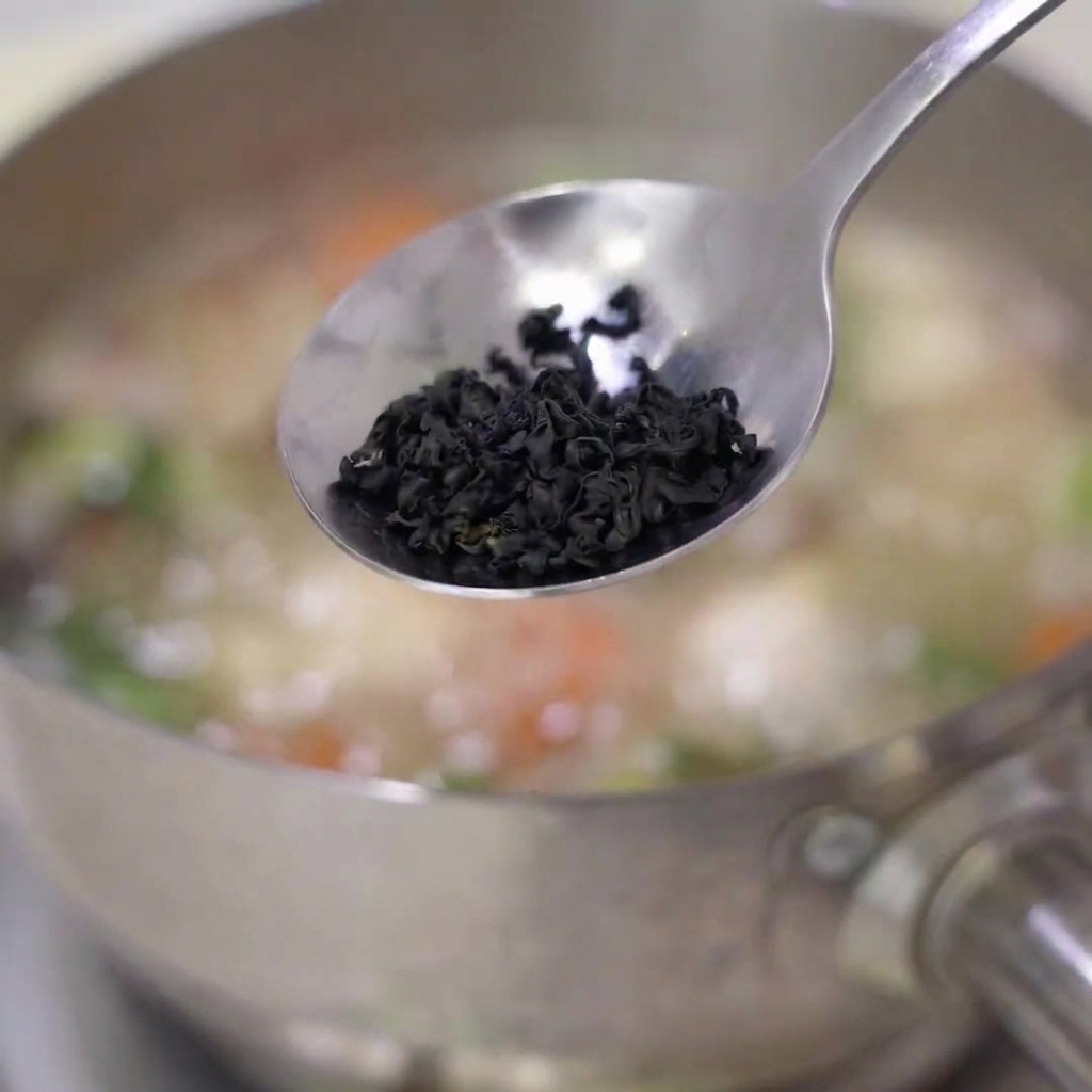 Getrocknete Wakame-Algen, die in einen Topf mit köchelnder Suppe gegeben werden.