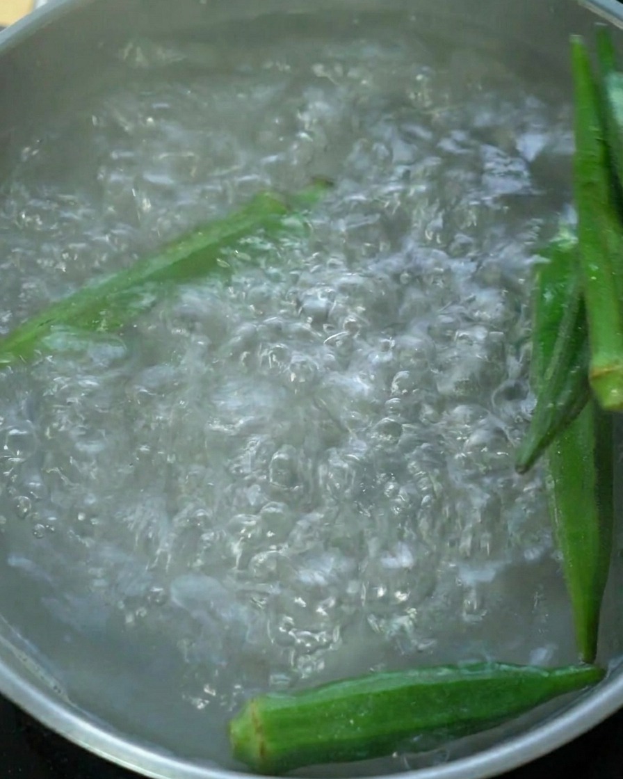 Frische grüne Okraschoten, die in einem Topf mit Wasser kochen.