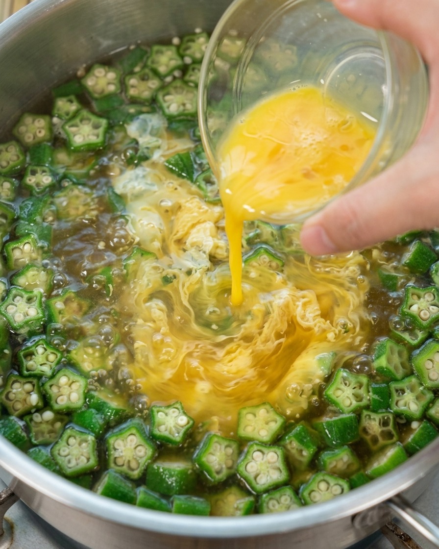 Geschlagenes Ei wird in die kochende Okrasuppe gegossen, um Fäden zu ziehen.