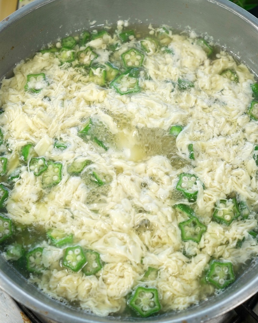 Okra-Eierstichsuppe im Topf, in die Salz eingerührt wird, bereit zum Servieren.