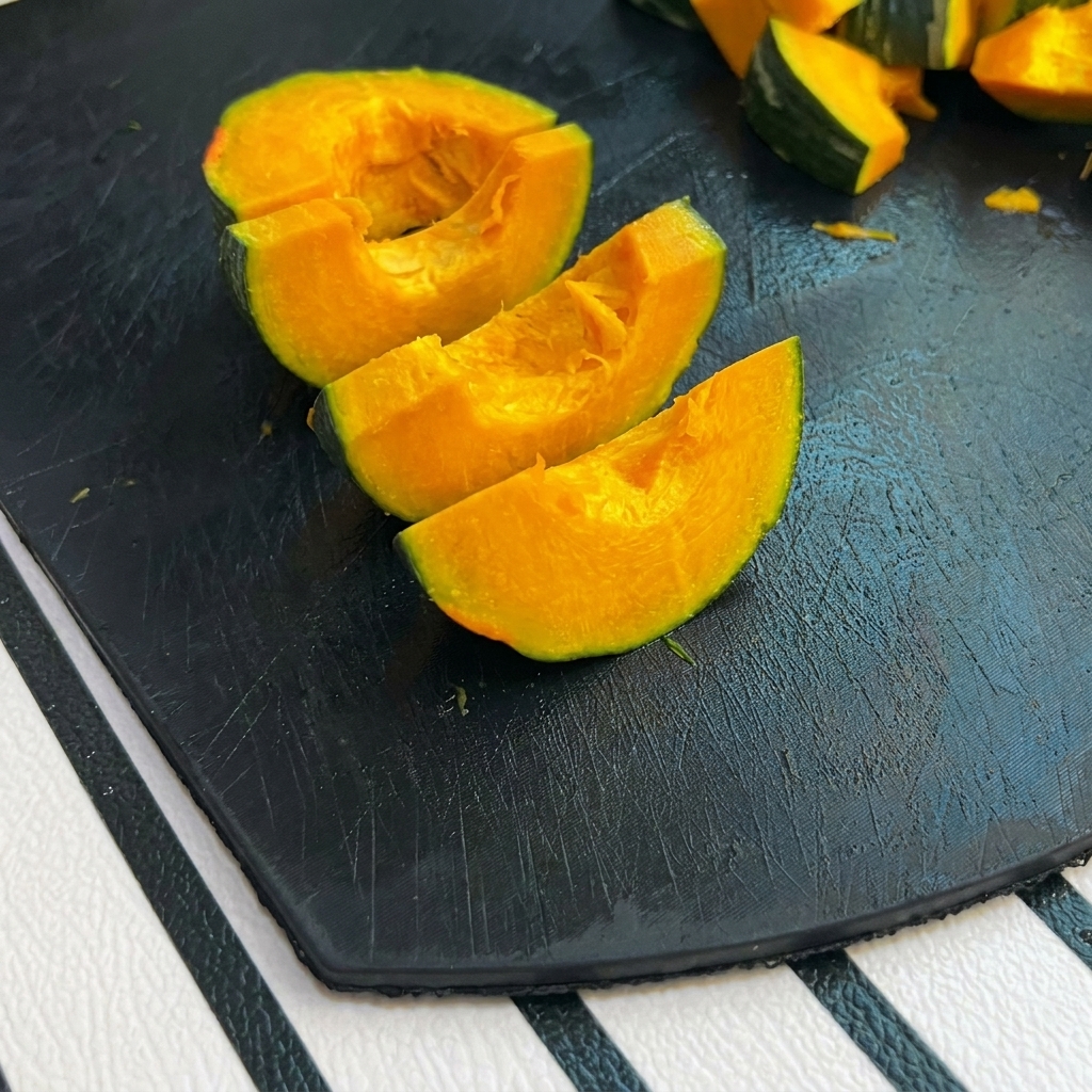 Kleine Stücke von grünem Kürbis auf einem schwarzen Schneidebrett.