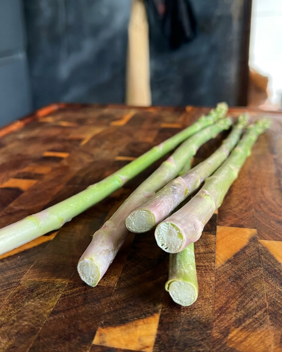 Nahaufnahme von frischem grünem Spargel, bei dem die holzigen Enden auf einem Holzbrett abgeschnitten werden.