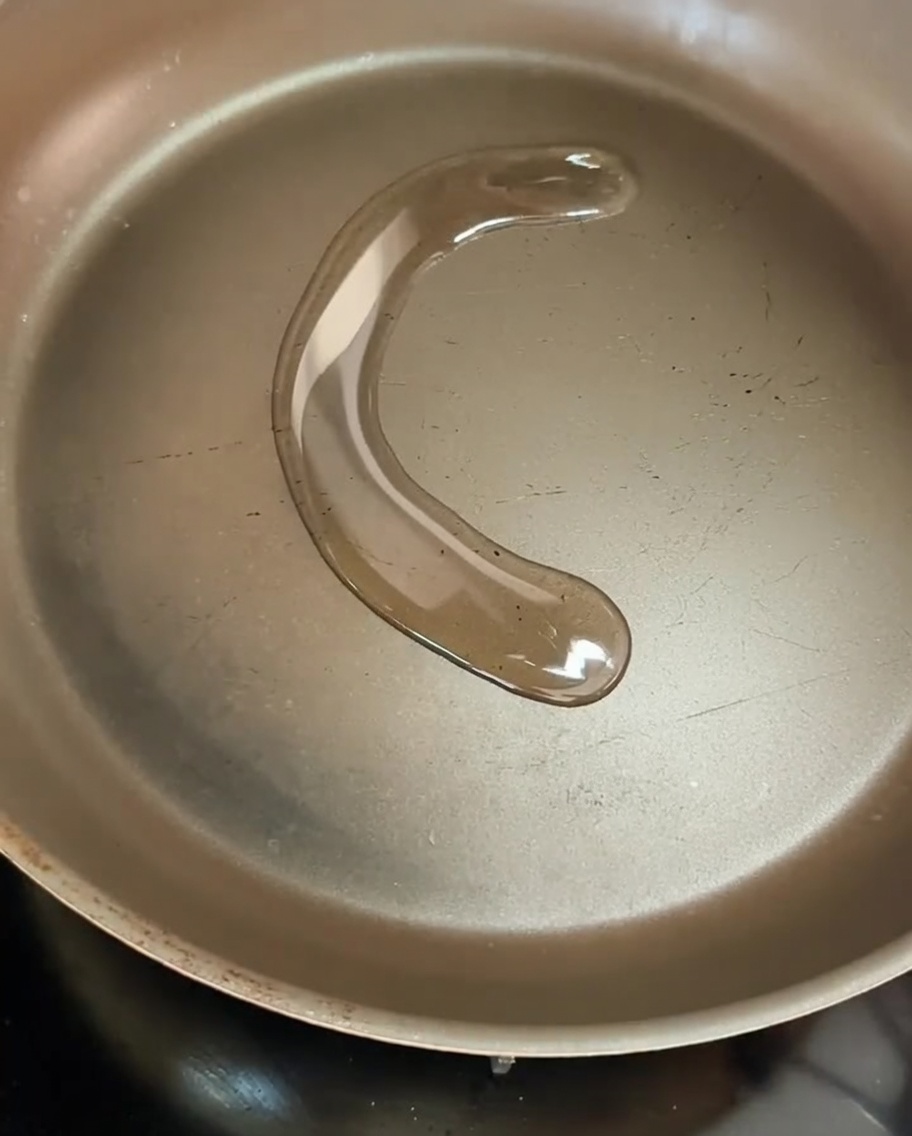 In Olivenöl brutzelnde Zwiebelringe in einer Pfanne, die leicht bräunen.