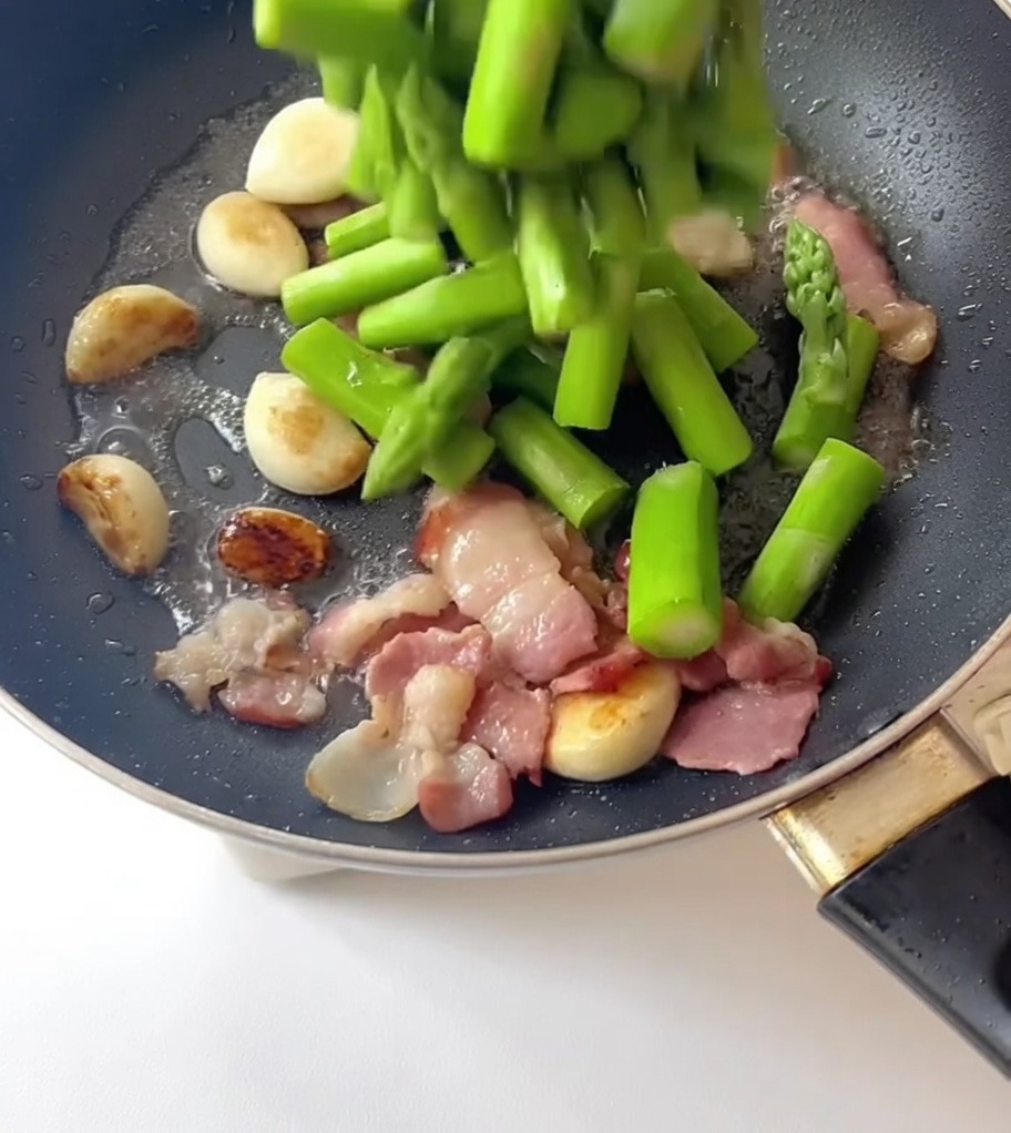 Blanchierte Spargelstücke werden in die Pfanne zu Knoblauch und Speck gegeben.