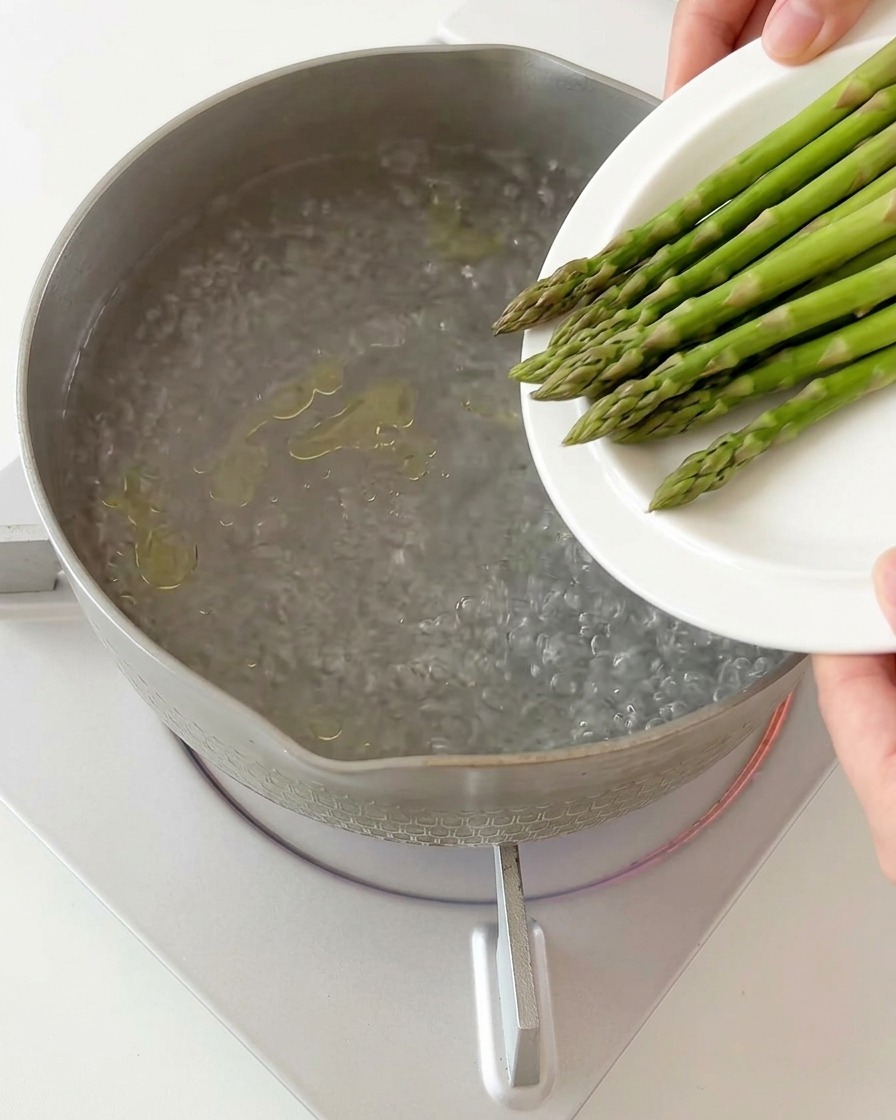 Geschnittene Spargelstücke werden in einen Topf mit kochendem Wasser gegeben.