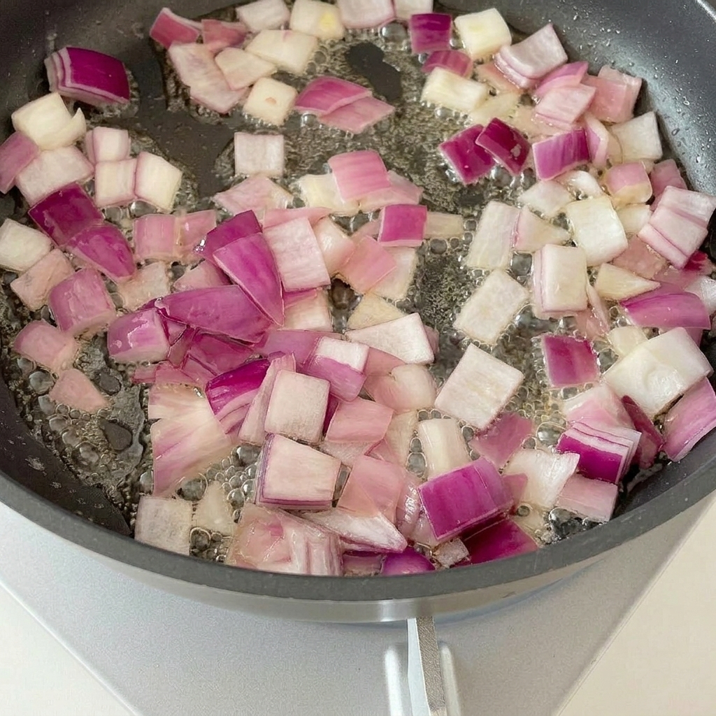Speckstücke braten in einer Pfanne mit angeschwitzten Zwiebeln.