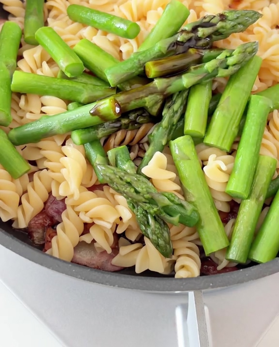 Soja- und Austernsauce werden über eine Pfanne voller Pasta, Speck und Spargel geträufelt.