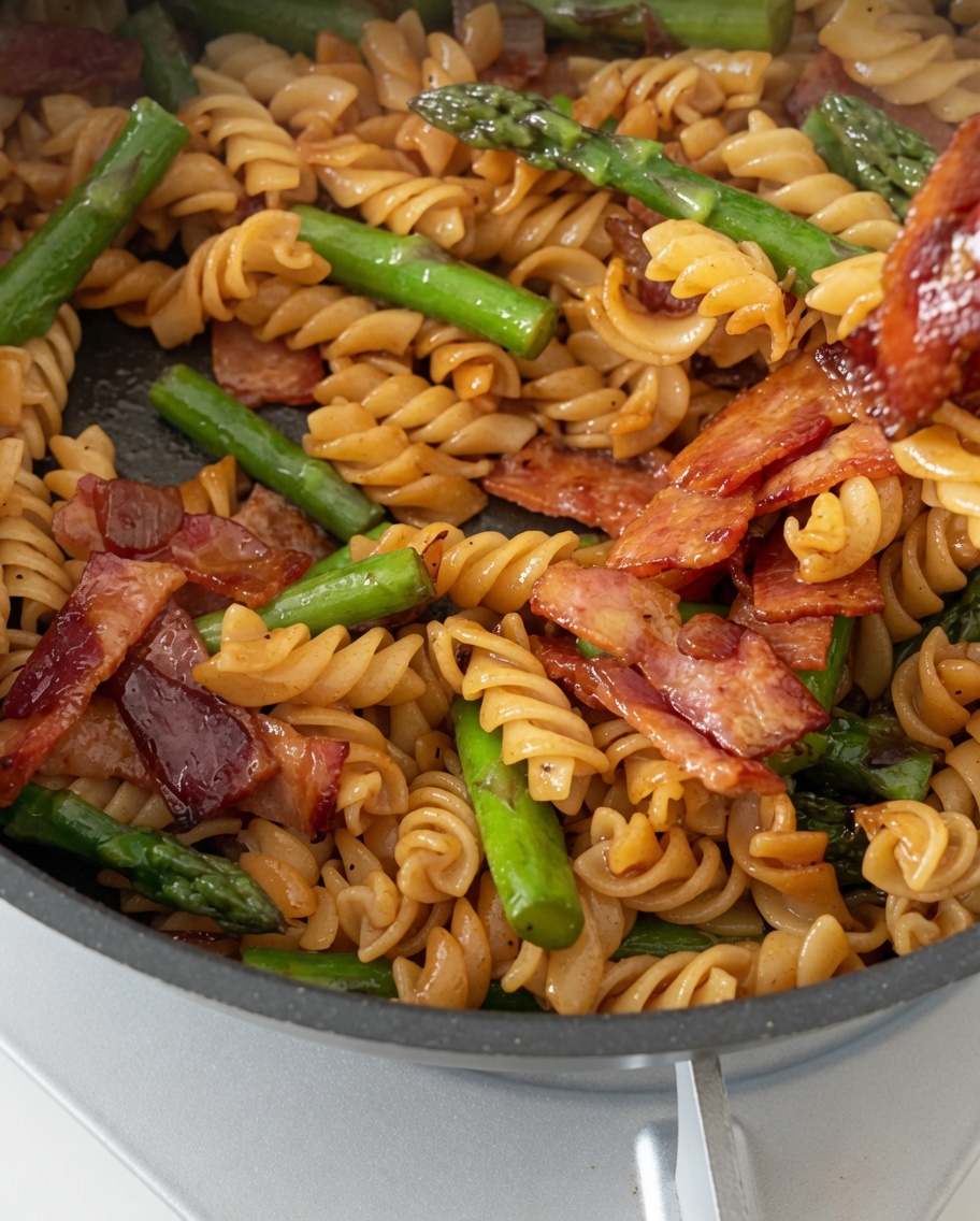 Eine Pfanne mit perfekt gekochten Fusilli, knusprigem Speck und zartem Spargel wird mit einer glänzenden herzhaften Sauce geschwenkt.