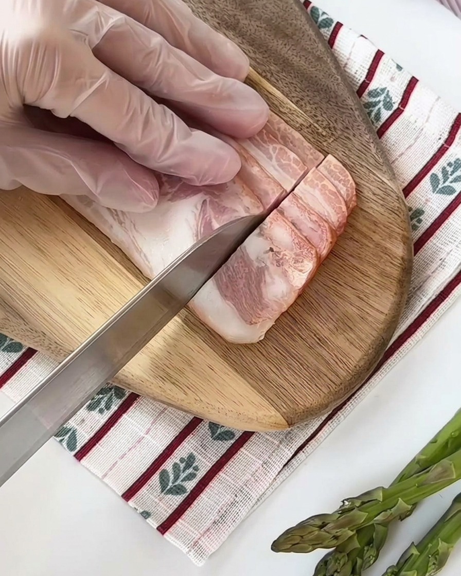 Rohe Speckstreifen werden auf einem Holzbrett in gleichmäßige kleine Quadrate geschnitten.