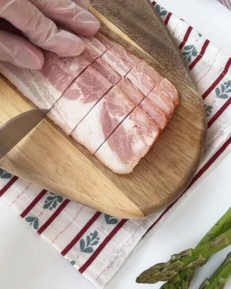Frische grüne Spargelstangen werden auf einem Holzbrett in gleich große Stücke geschnitten.