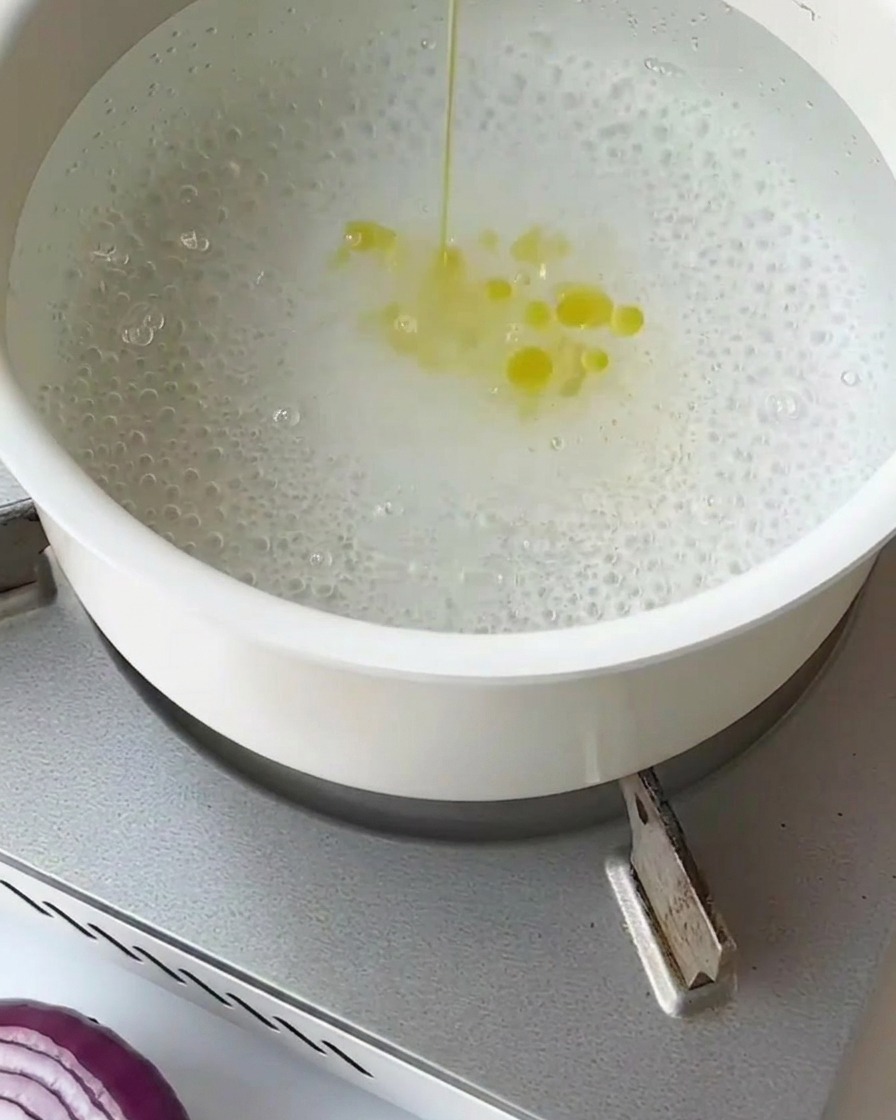 Spargelstücke werden in einem Metallsieb kurz in kochendem Wasser blanchiert.