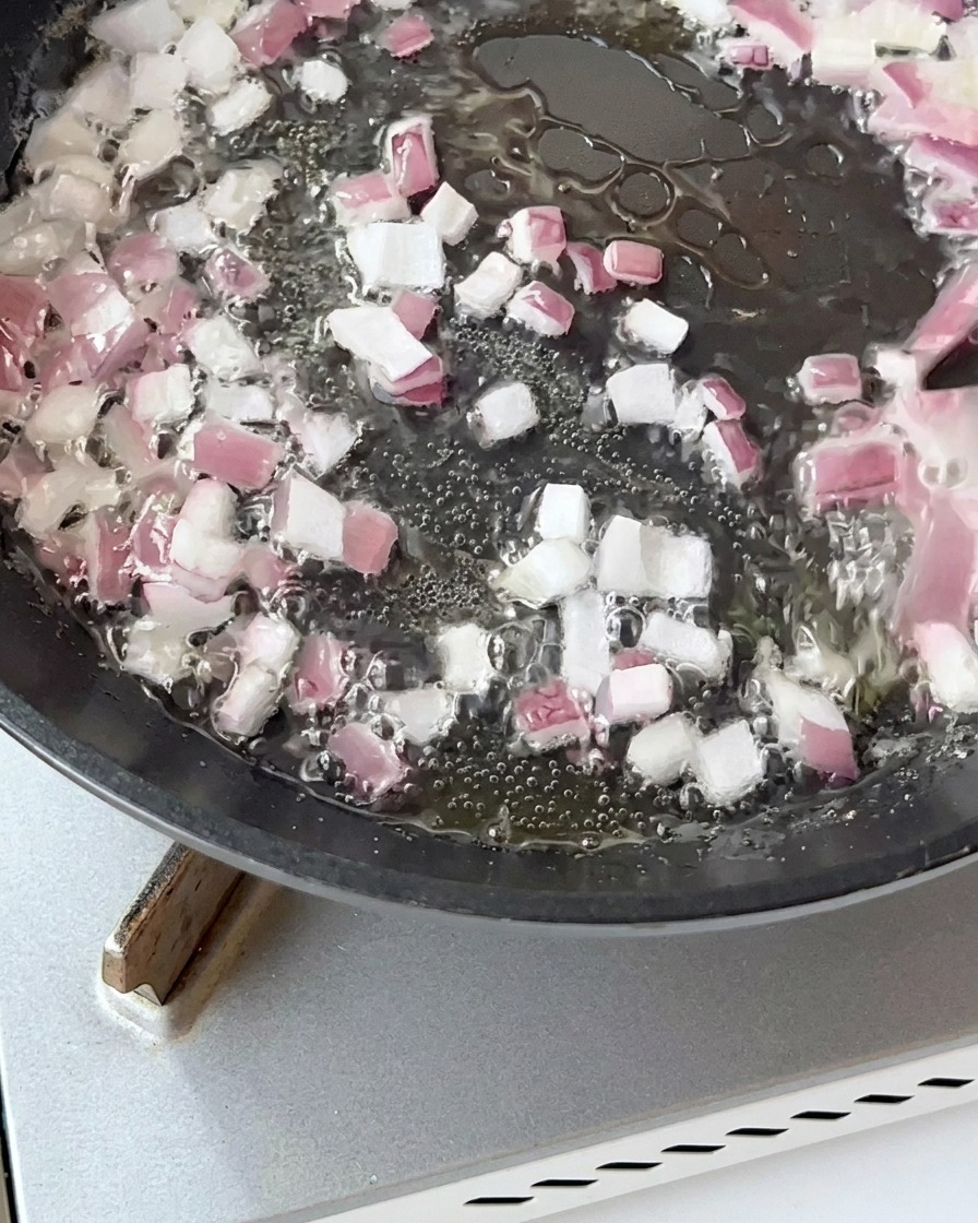 Speckstücke braten zusammen mit den Zwiebeln in der Pfanne goldbraun an.