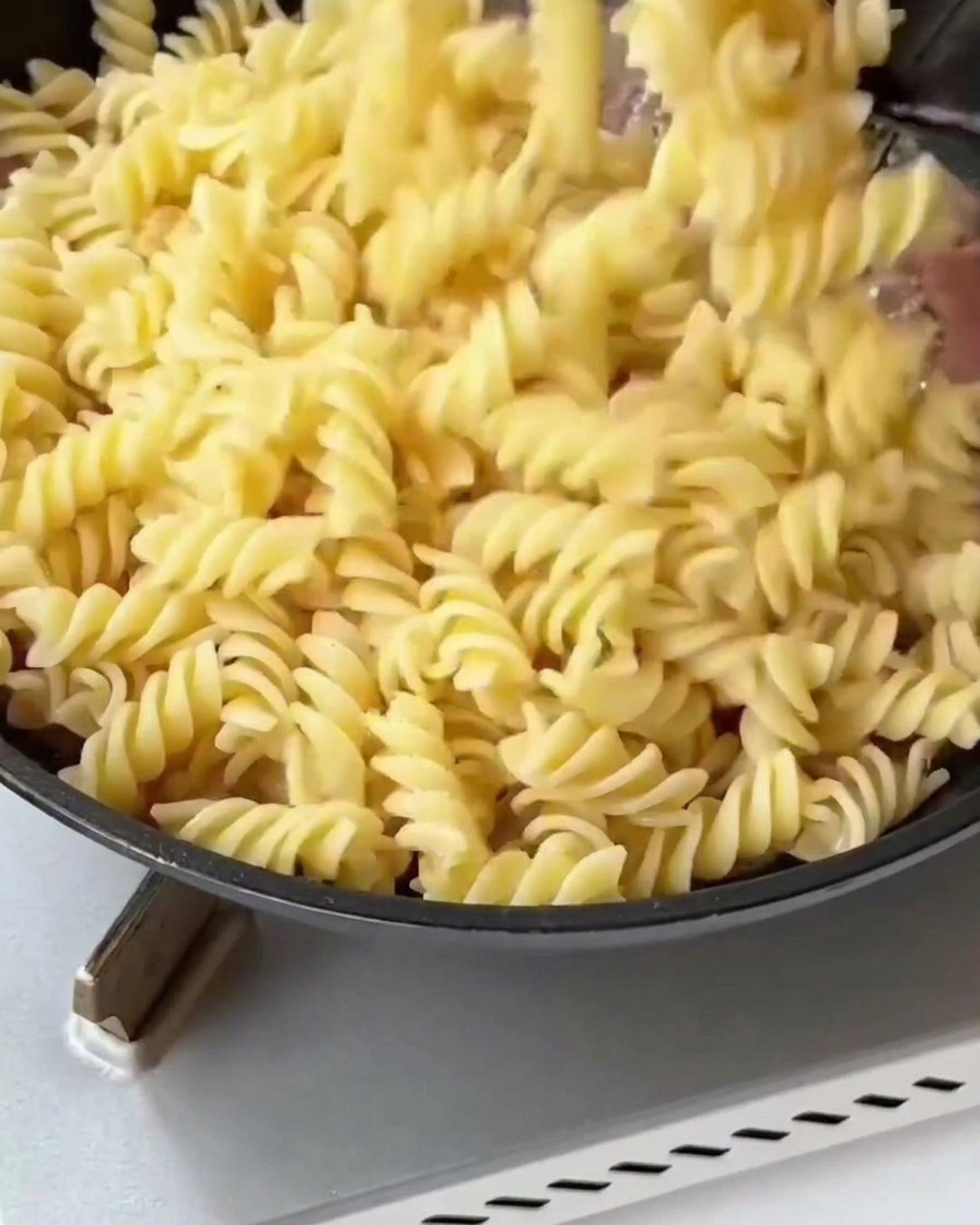 Gekochte Fusilli und blanchierter Spargel werden in die Pfanne zum gebratenen Speck gegeben.