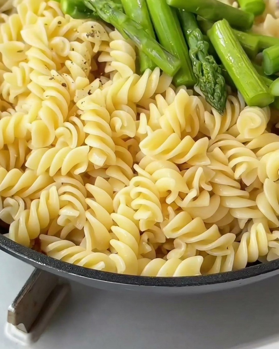 Fusilli und grüner Spargel in der Pfanne werden mit frisch gemahlenem schwarzem Pfeffer bestreut.