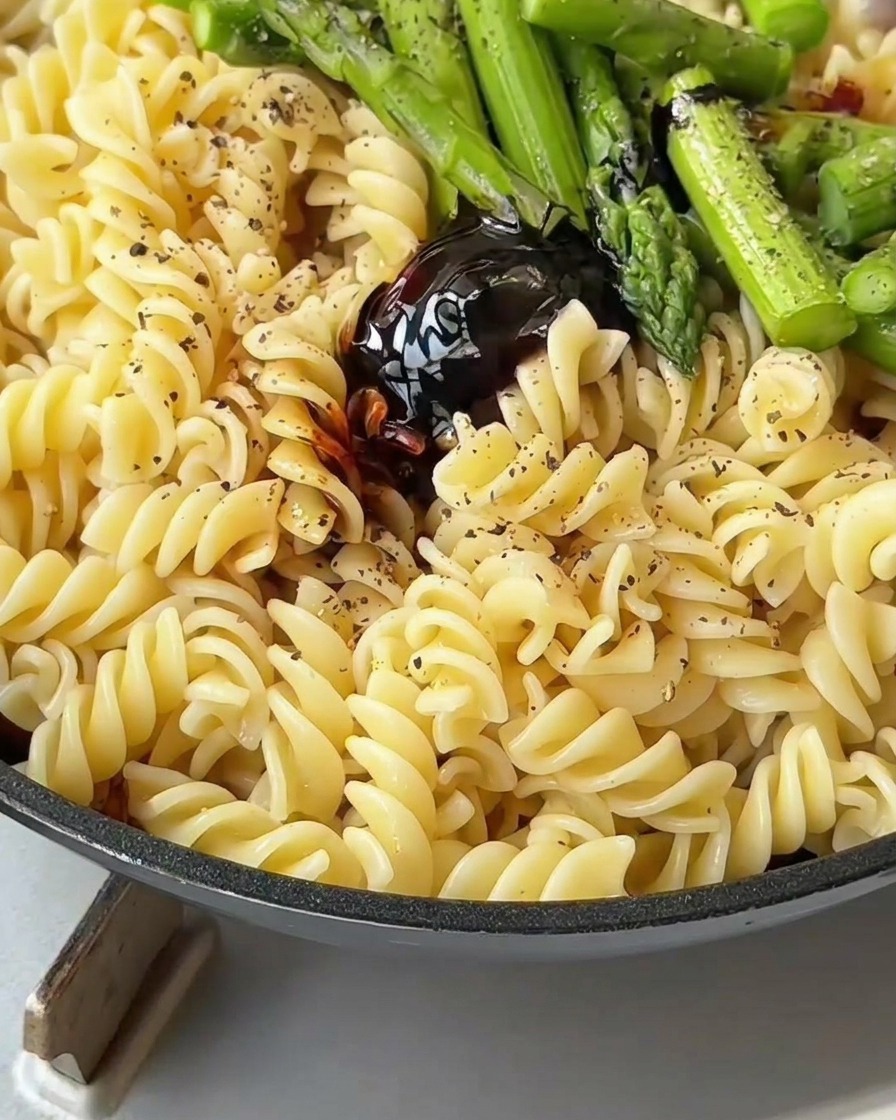 Pasta, Speck und Spargel werden mit einem Pfannenwender vermischt, damit sie gleichmäßig mit Sauce überzogen werden.