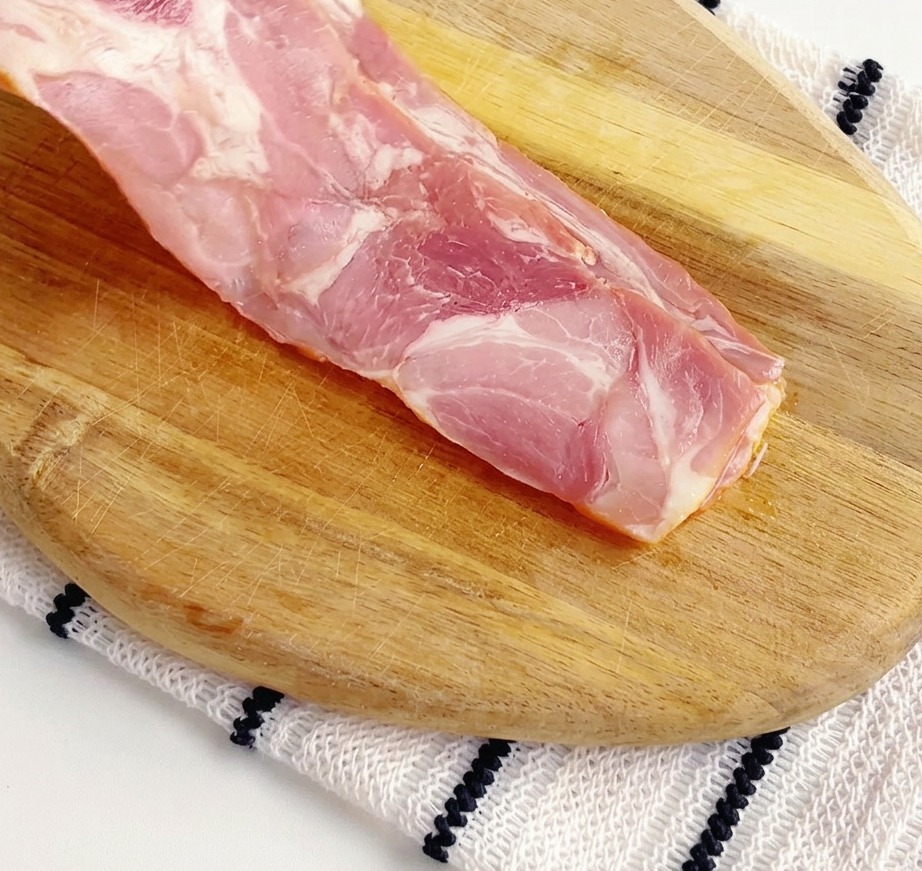 Roher Speck in kleinen Stücken auf einem Schneidebrett.