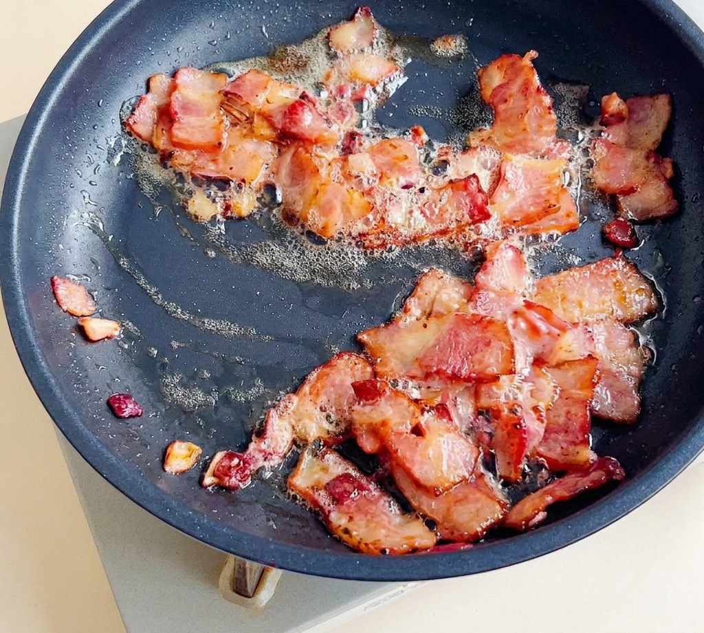 Speckstücke braten in der Pfanne mit den Zwiebeln.