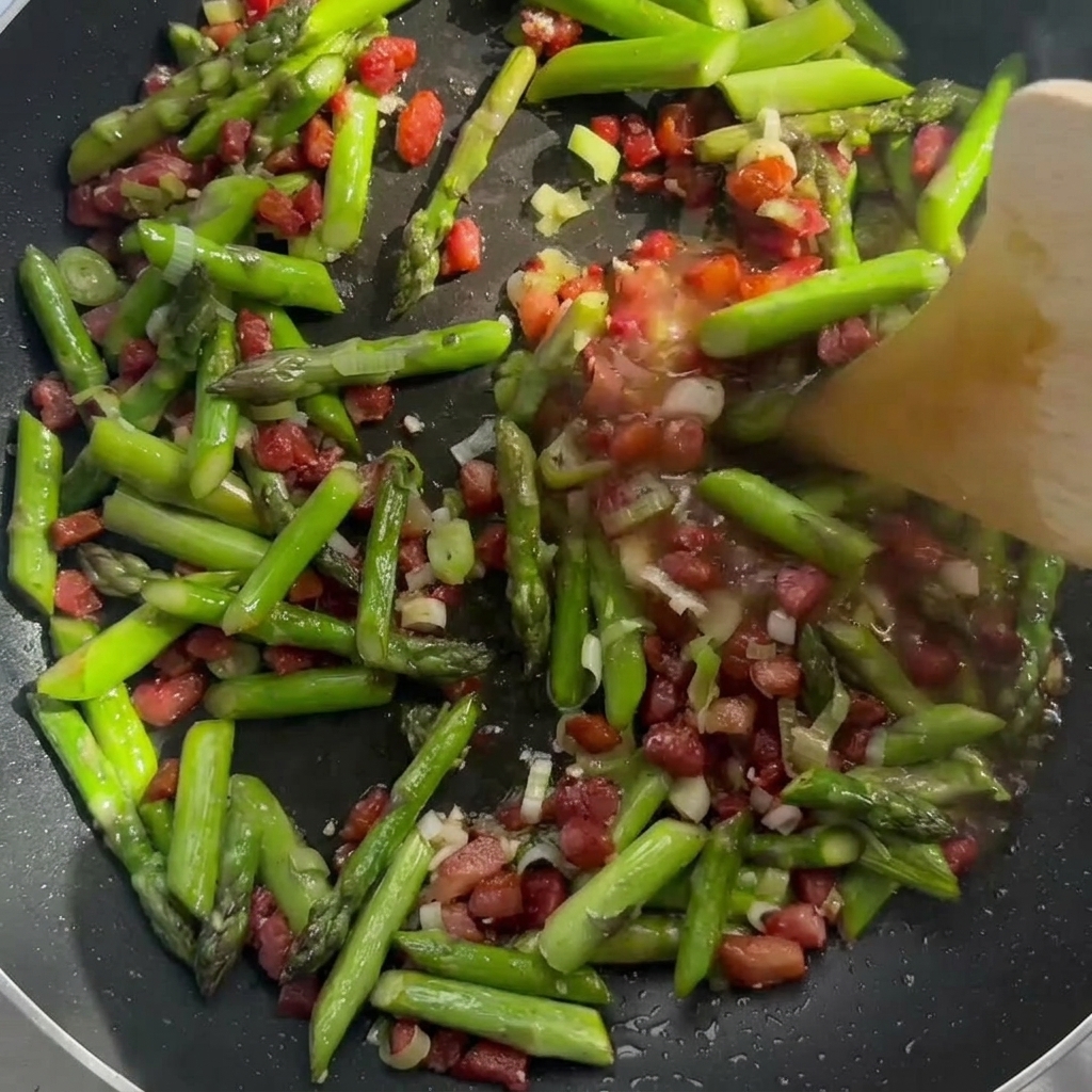 Sahne wird zu dem Speck und Spargel in die Pfanne gegeben.