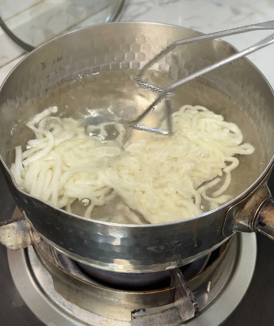 Gekochte Udon-Nudeln werden mit einem Sieb aus dem kochenden Wasser gehoben.