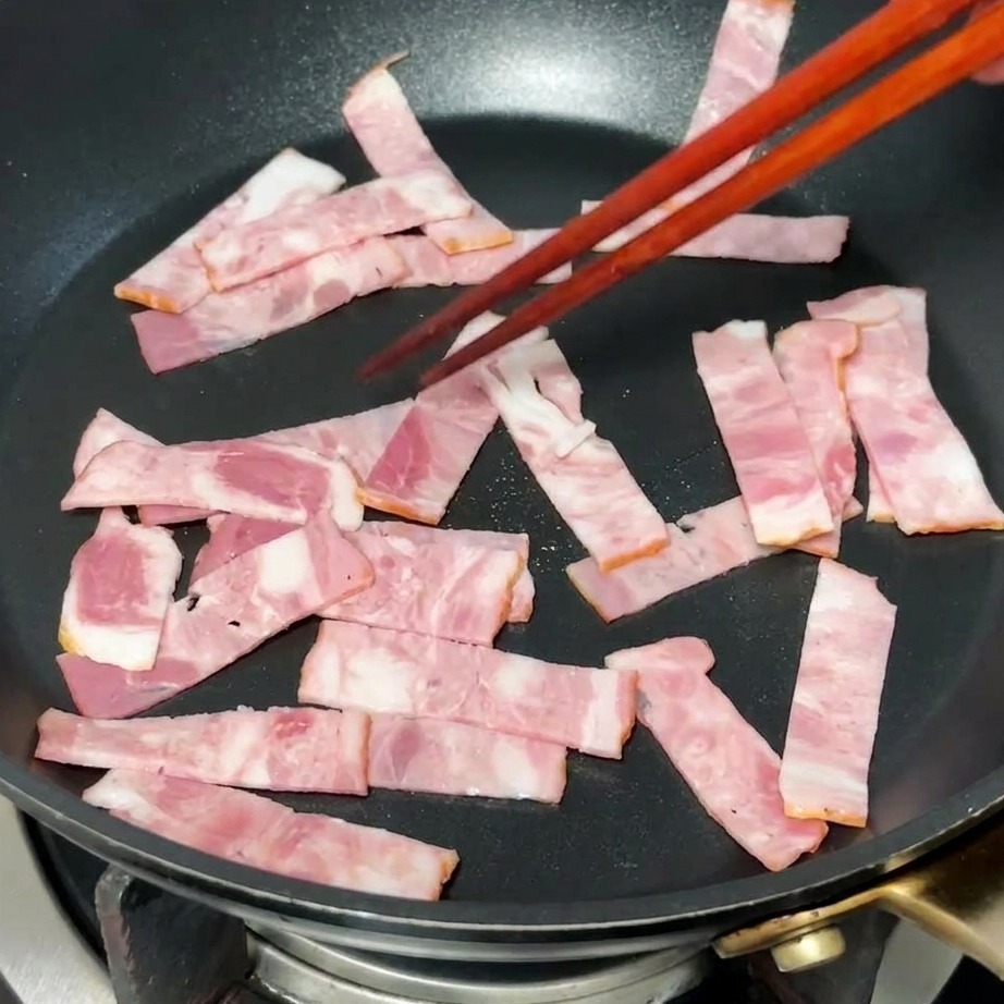 Speckstücke braten in einer heißen Pfanne, das Fett tritt aus.