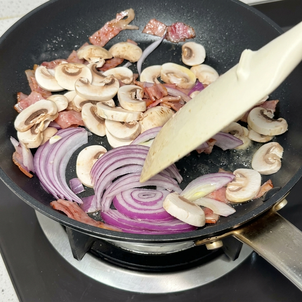 Geschnittene rote Zwiebeln und Pilze werden mit Speck und Butter angebraten.