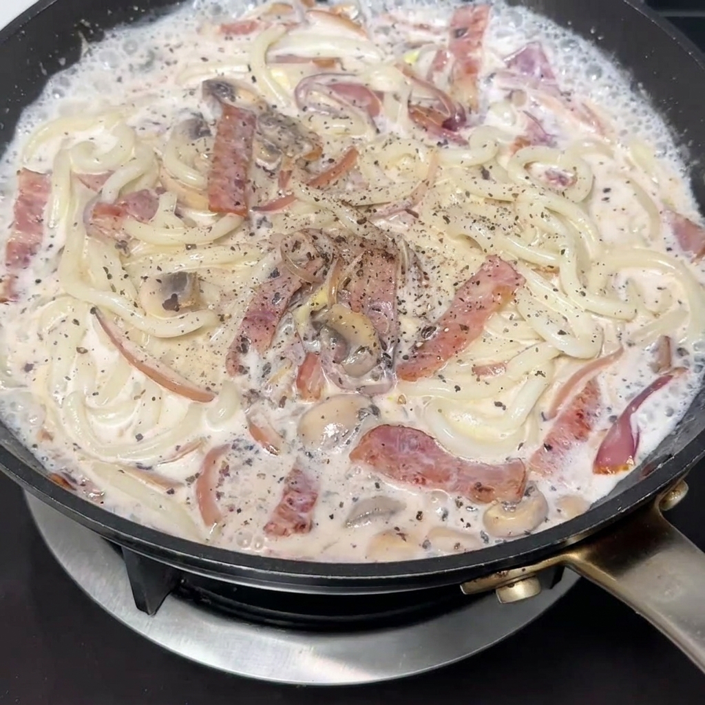 Frisch gemahlener schwarzer Pfeffer wird über die Udon-Pfanne gestreut.