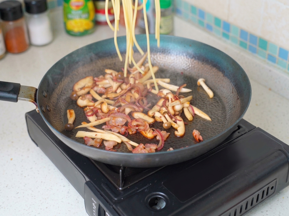 Gekochte Angel Hair Pasta wird in die Pfanne mit den angebratenen Zutaten gegeben.