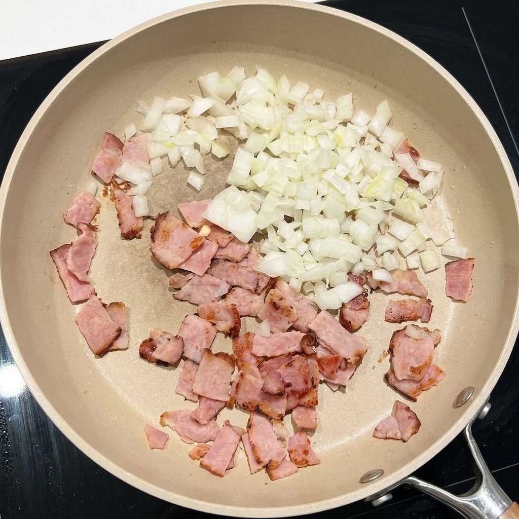 Gehackte weiße Zwiebeln werden mit Speckstücken in einer großen Pfanne angebraten.