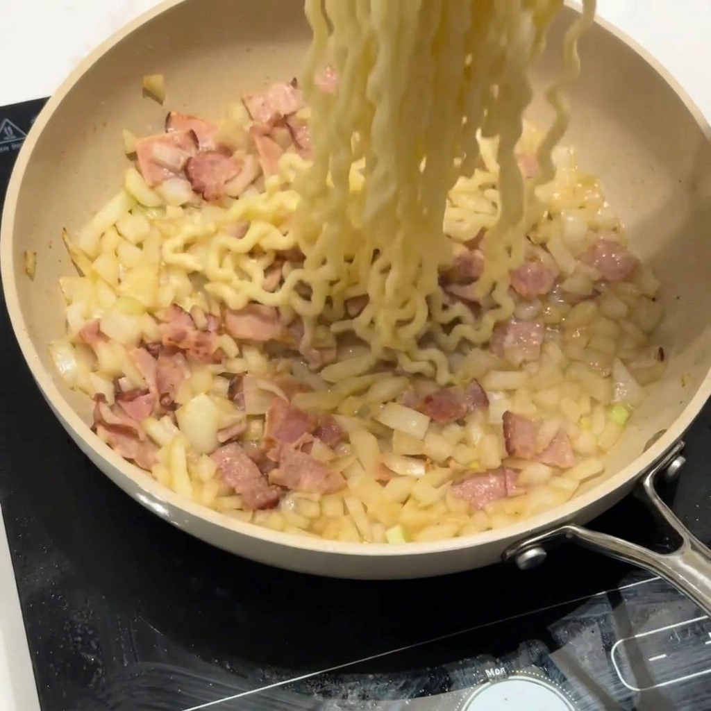 Lockennudeln werden in die Pfanne zu Speck und Zwiebeln gegeben.