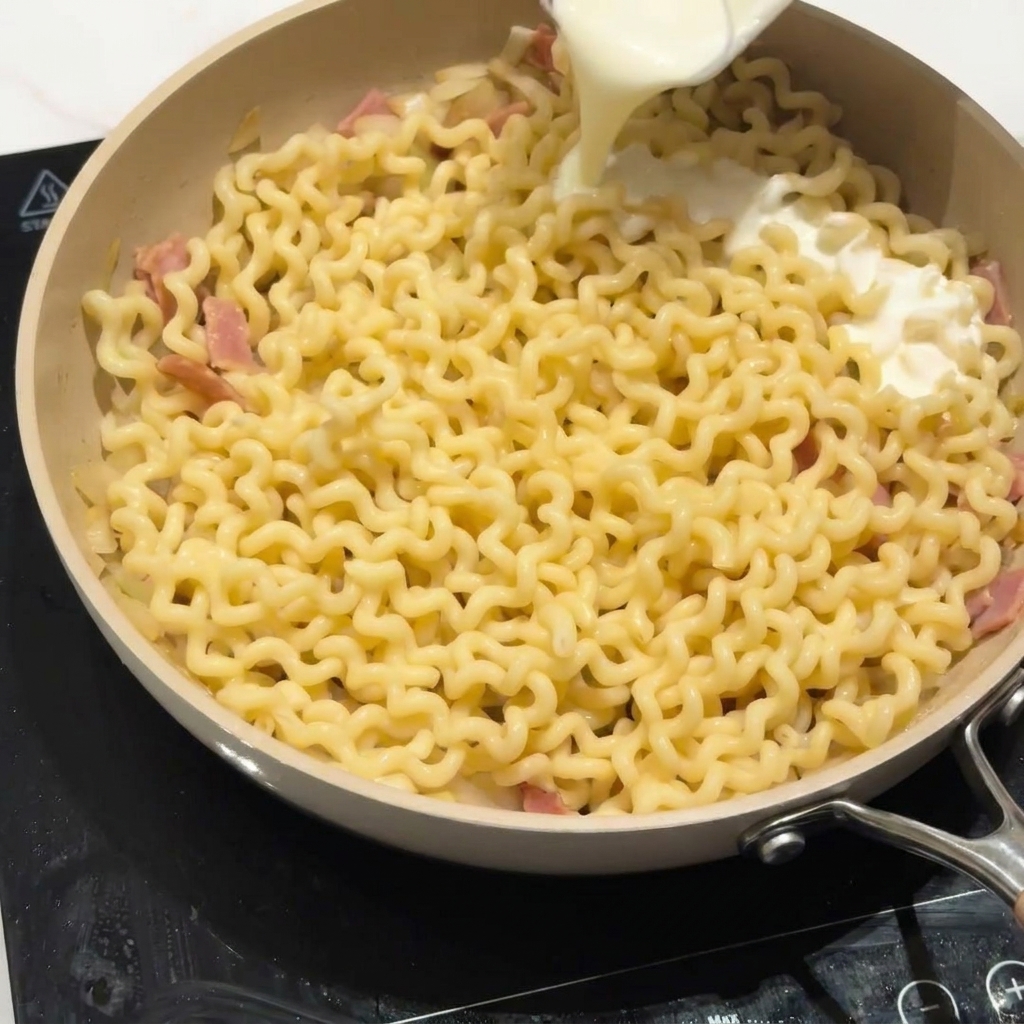 Fettarme Milch wird über die Nudeln in der Pfanne gegossen.