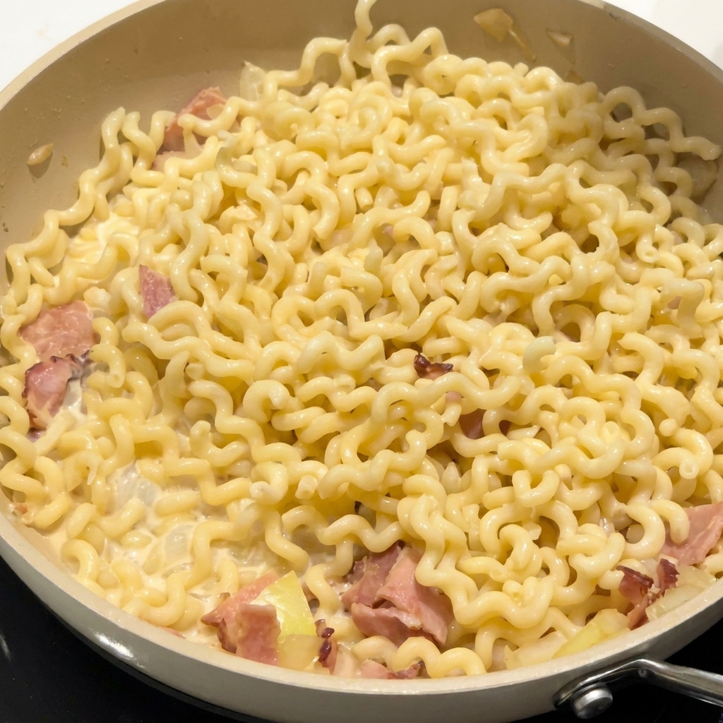 Gewürze werden über die Nudeln und den Speck in der Soße gestreut.