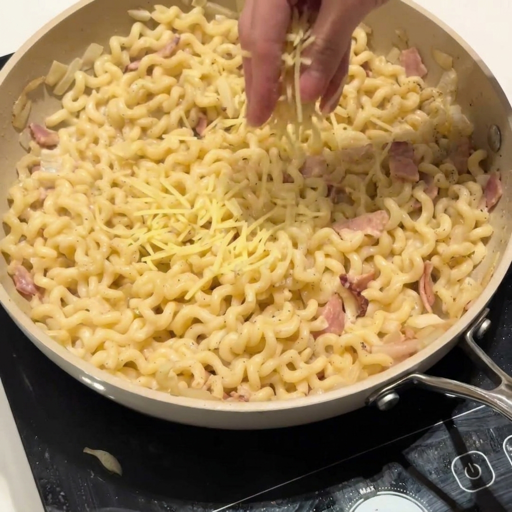 Parmesan wird über die cremige Pasta in der Pfanne gestreut.