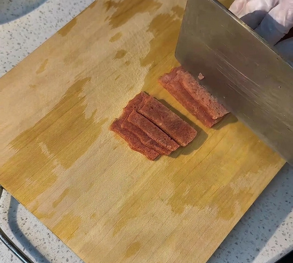Rohe Speckscheiben ordentlich auf einem Holzbrett für die Zubereitung angerichtet.