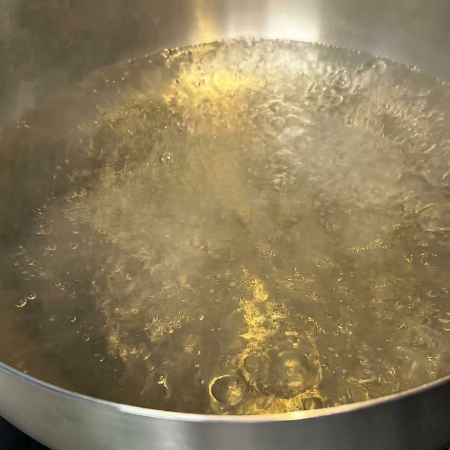 Ein Topf mit kochendem Wasser und ein paar Tropfen Öl an der Oberfläche.
