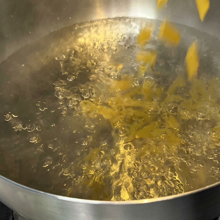 Penne-Nudeln werden in einen Topf mit sprudelnd kochendem Wasser geschüttet.