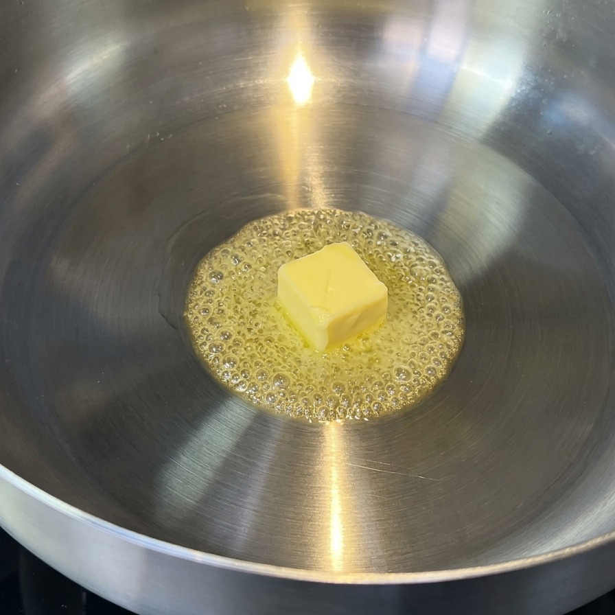 Butter schmilzt in einer Edelstahlpfanne und wirft leicht goldene Bläschen.