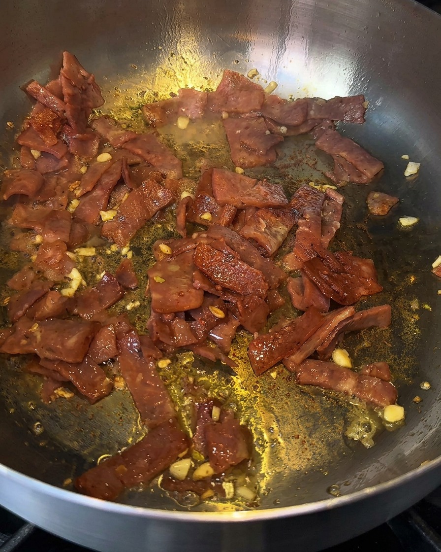 Zischender Speck und Knoblauch in einer Pfanne, die mit einem Schuss Kochflüssigkeit abgelöscht werden.